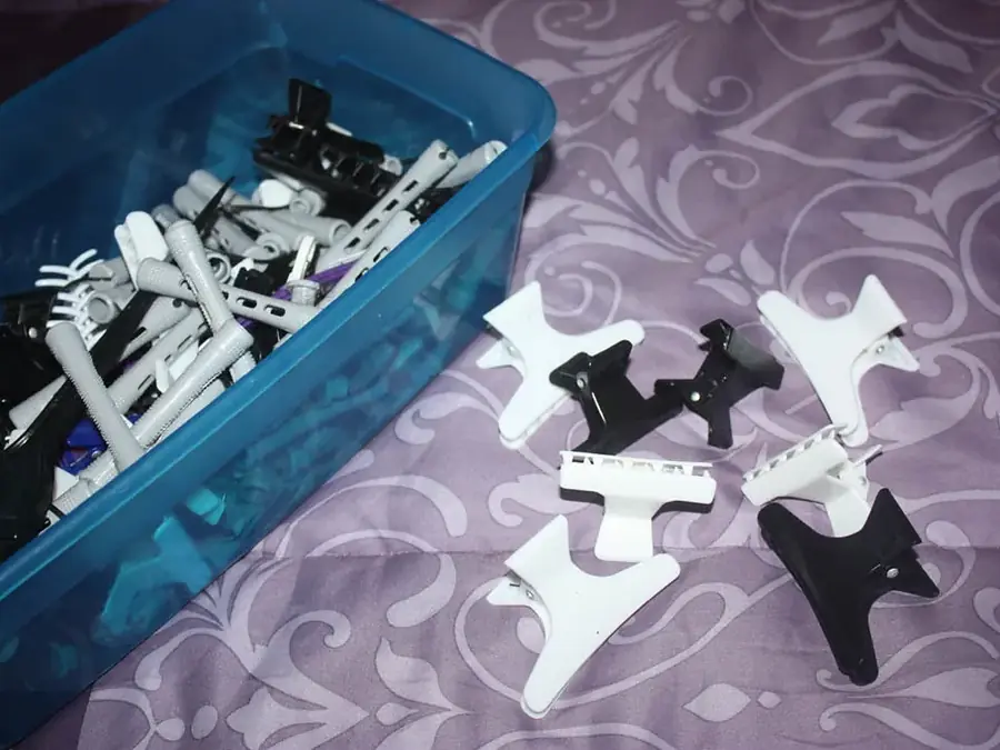 Black and white claw clips with toothed jaws spread across a lilac patterned cloth beside a blue tub